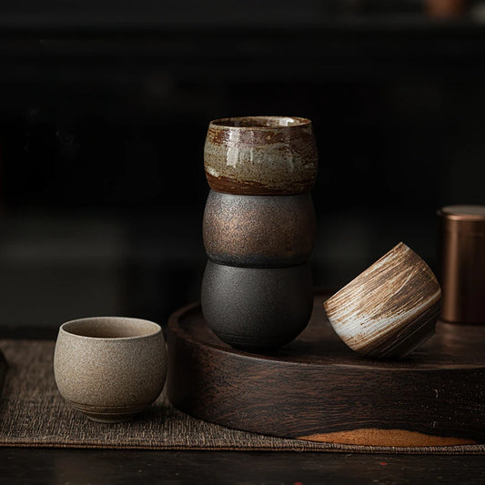 Stack of ancient style small tea coffee cup set in earthy tones on wooden tray with dark background